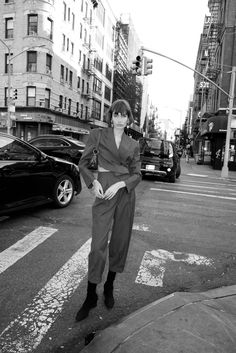 a woman standing on the side of a road next to traffic lights and parked cars