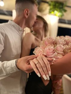 a man and woman kissing each other while holding pink roses in their hands with candles behind them