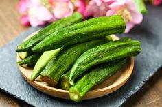 a wooden bowl filled with cucumbers on top of a table next to flowers