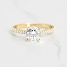 a yellow gold engagement ring with diamonds on the band and a single round diamond in the center