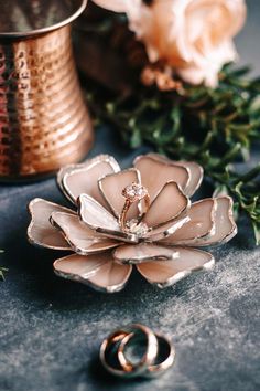 two wedding rings sitting on top of a flower shaped broochle next to some greenery