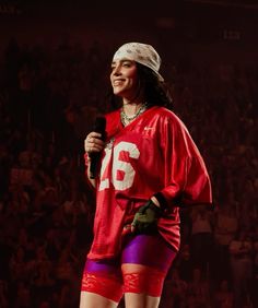 a woman in red and purple outfit holding a microphone while standing next to a crowd