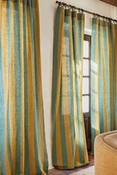 a living room with yellow and green striped curtains on the window sill, brown chair, and ottoman