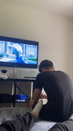 a man sitting in front of a flat screen tv with his feet on the bed