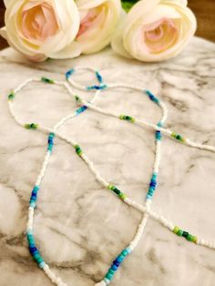 two white roses sitting on top of a table next to a blue and green beaded necklace