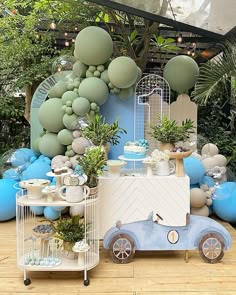 a blue and white dessert cart with balloons on the wall behind it in front of trees