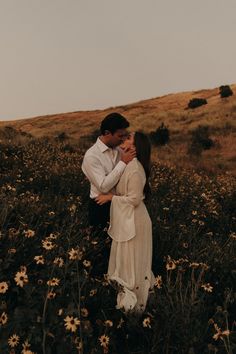 a man and woman embracing in a field of wildflowers with the sky above them