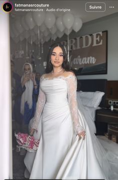 a woman in a white wedding dress standing next to a bed with balloons hanging from the ceiling