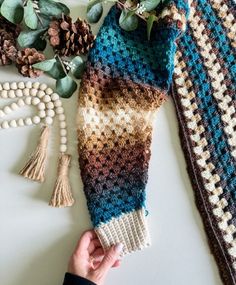 a person is holding a knitted scarf next to other crocheted items and flowers