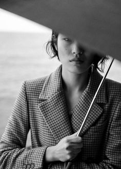 a woman holding an umbrella over her head while standing next to the ocean in black and white