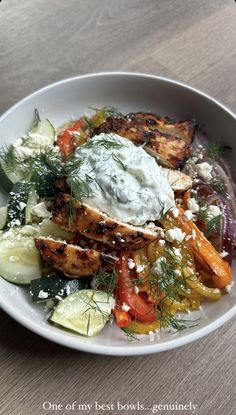 a white bowl filled with lots of food on top of a wooden table next to a fork