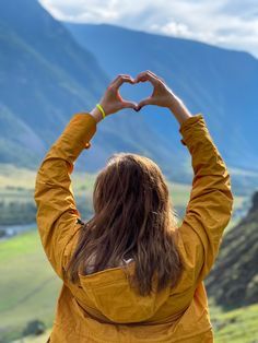 a woman making a heart shape with her hands on top of the mountain overlooking a valley