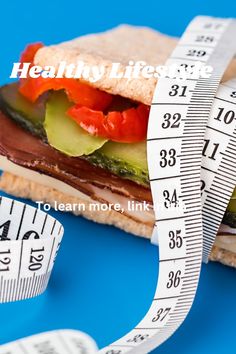 a sandwich with tomatoes, cucumber and lettuce on it next to a measuring tape