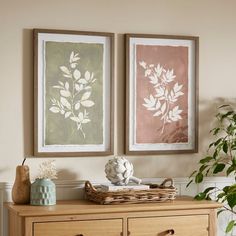 two paintings on the wall above a dresser in a room with plants and vases