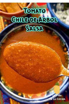 a spoon full of tomato sauce on top of a bowl with the words tomato chile de arbol salsa