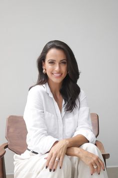 a woman sitting on top of a wooden chair next to a white wall and smiling