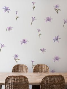 a dining room table with wicker chairs and purple flowers on the wall behind it