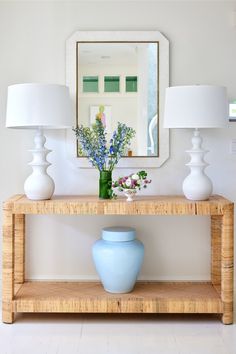 a blue vase sitting on top of a wooden table next to two lamps and a mirror