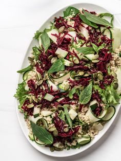 a white plate topped with a salad covered in greens and cucumber slices on top of rice