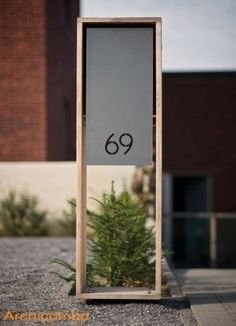 a tall wooden sign sitting on the side of a road next to a small tree