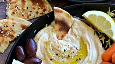 hummus, carrots, and pita bread are served in black bowls on a wooden table