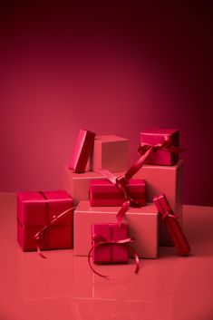 several pink boxes with red ribbons and bows are stacked on top of each other in front of a magenta background