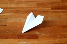 two origami airplanes sitting on top of a wooden floor