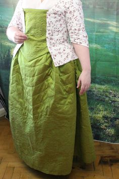 a woman standing in front of a painting wearing a green dress and white shirt with flowers on it