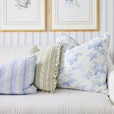 four pillows on a white couch with blue and green striped wallpaper