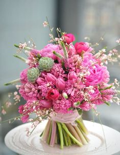 a bouquet of pink flowers sitting on top of a white cake plate with succulents