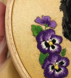 a close up of a person's hand holding a cross stitched purple flower