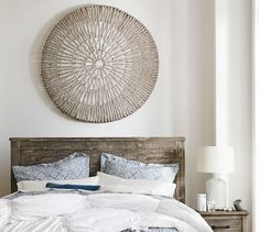 a bed with white sheets and pillows in front of a wall hanging on the wall