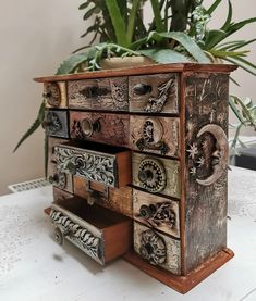 an old dresser with drawers is sitting on a table next to a potted plant