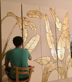 a man sitting on a chair in front of a wall with leaves painted on it