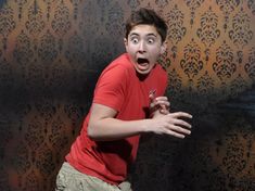 a young man making a surprised face while standing in front of a wall