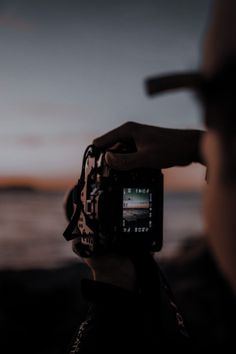 a person holding a camera up to their face with the sun setting in the background