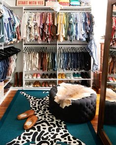 a walk in closet with clothes and shoes on the floor next to an ottoman that has a cowhide footstool