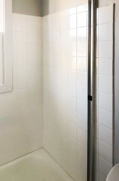 a white tiled bathroom with a shower and toilet in the corner, next to a window