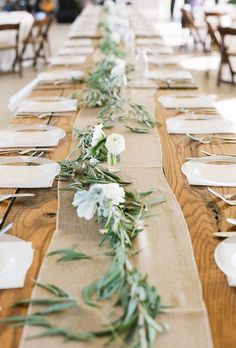 the long table is set with white flowers and greenery on each placemats