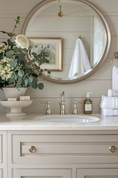 a bathroom sink with flowers in a vase on it and a mirror above the sink