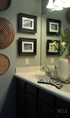 a bathroom sink with three framed pictures on the wall above it and a vase filled with flowers