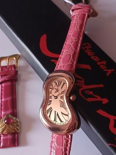 a pink watch sitting on top of a table next to a red wrist strap and a black box