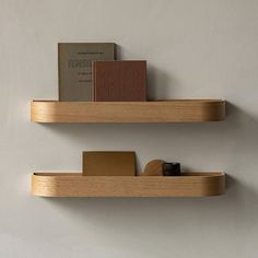 two wooden shelves with books on them against a white wall, one shelf has a book and the other is empty