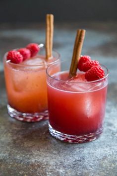 two glasses filled with drinks and garnished with cinnamon sticks, raspberries