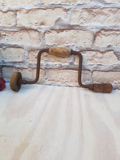 an old rusty pipe is on the floor next to a brick wall with flowers in it