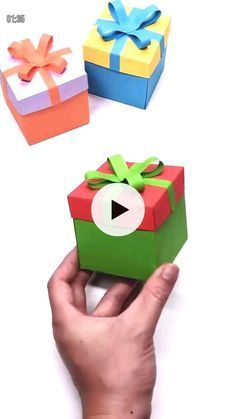 someone is holding an origami gift box with a video coming out of it