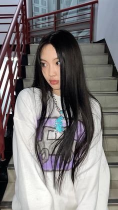 a woman with long black hair standing in front of stairs