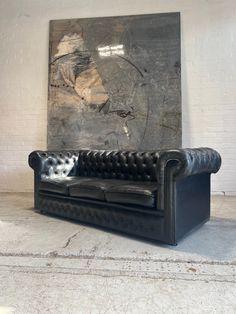 a black leather couch sitting in front of a large piece of art on the wall