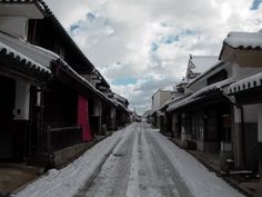 an empty street with snow on the ground and buildings in the background, under a cloudy sky