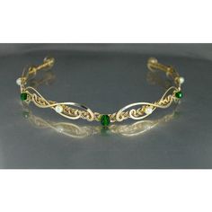 a gold bracelet with green stones and leaves on the front, sitting on a gray surface